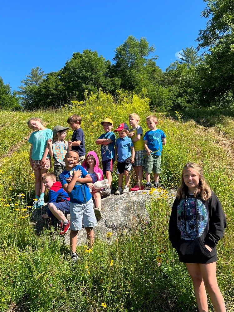 SummerCampYouth_2022 A group of elementary school students in a field of green grass under a blue summer sky